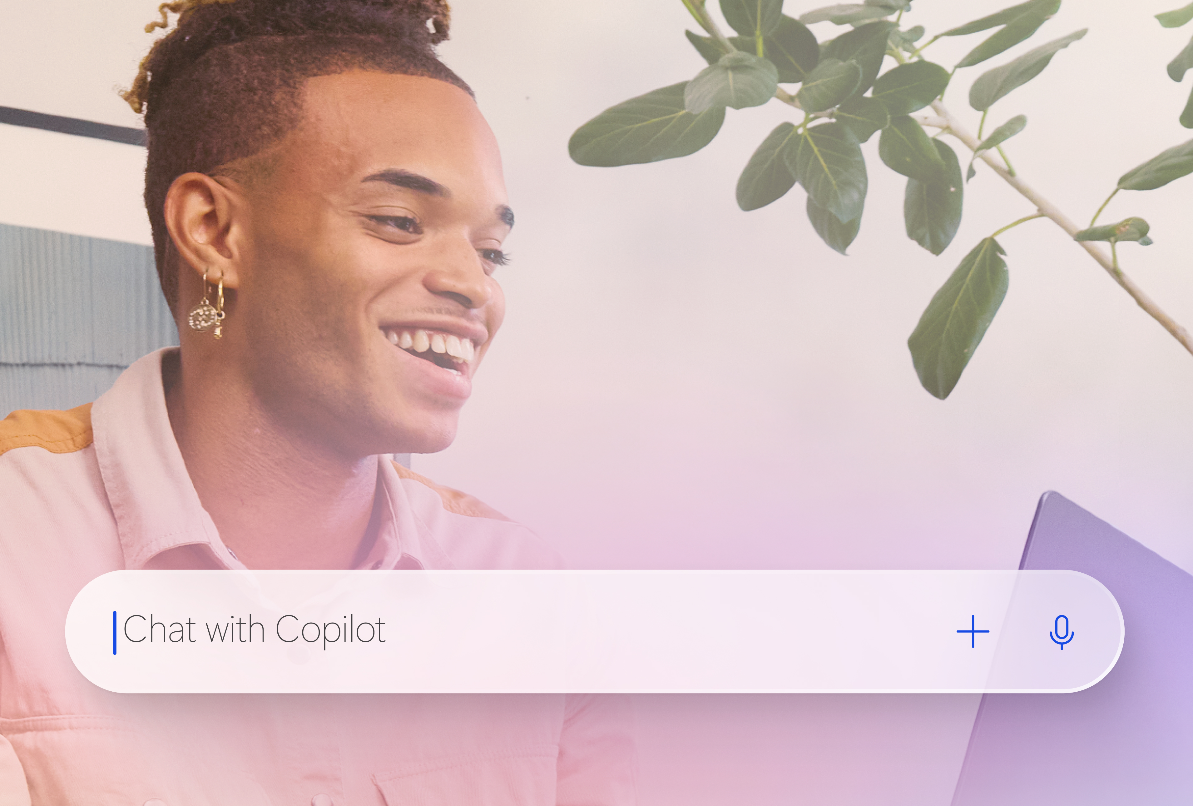A smiling man sitting and looking at an open laptop with an enlarged Copilot search bar overlaid at the bottom